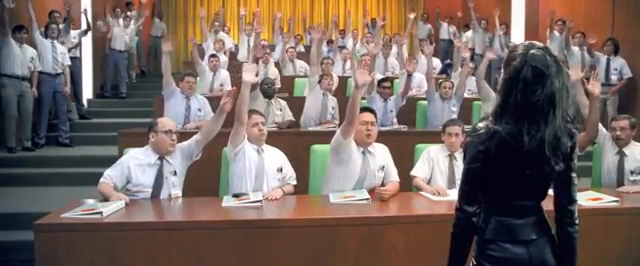 A room of men in business casual attire raising their hands in front of their teacher.